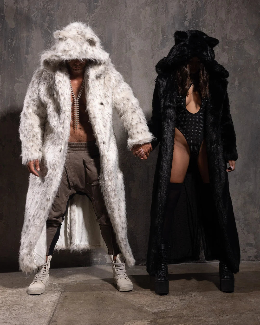 Two people wearing long fur coats, one white and one black, against a gray background.