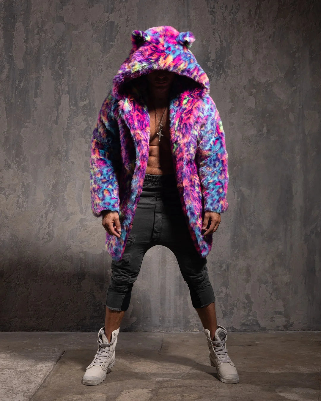 Person wearing a colorful neon leopard print faux fur coat with an oversized hood with ears, against a gray textured wall.