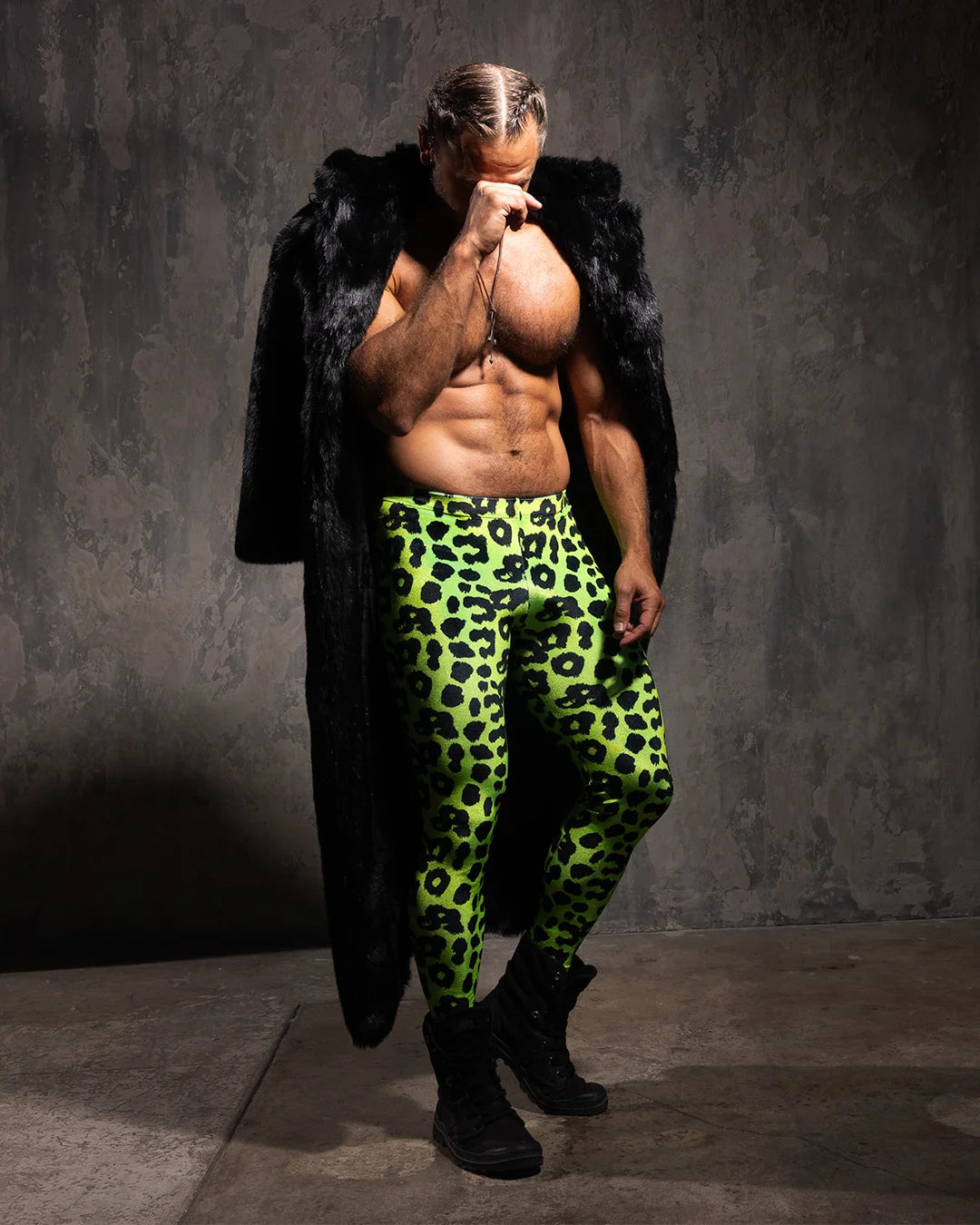 Man wearing neon green leopard print velvet leggings and a black panther fake fur floor length coat against a gray background