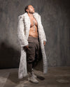 Man wearing a long white snow leopard fake fur coat over minimal clothing against a textured gray background
