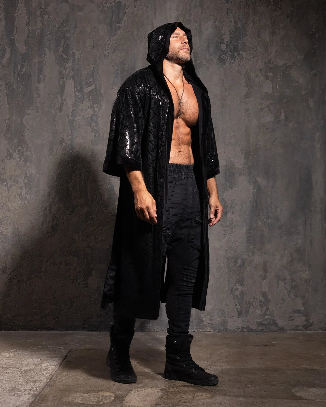 Man wearing a black hooded kimono with sequin black snakeskin pattern against a textured gray wall