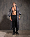 Man wearing a long, sequin kimono robe with silver and gold leopard print over black pants against a textured gray wall.