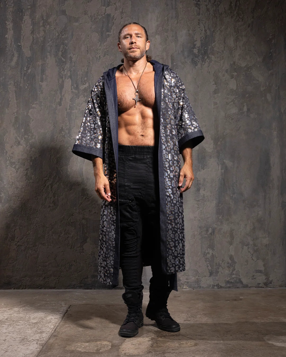 Man wearing a long, sequin kimono robe with silver and gold leopard print over black pants against a textured gray wall.
