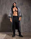 Man wearing a long, silver sequin kimono over a black outfit against a textured gray wall.