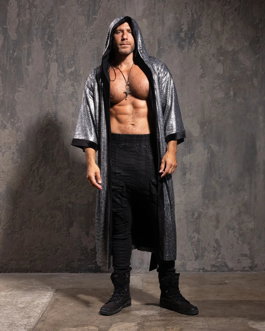 Man wearing a long, silver sequin kimono over a black outfit against a textured gray wall.