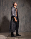 Man wearing a long, denim-colored hooded kimono with sequin leopard print details against a textured gray wall.