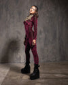 A Woman wearing a red leopard print burnout velvet full bodysuit with platform boots against a textured gray wall.