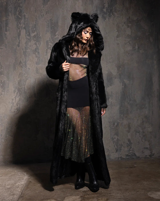 Model wearing a long floor length black fake fur coat with hood andears and colorful skirt against a dark background