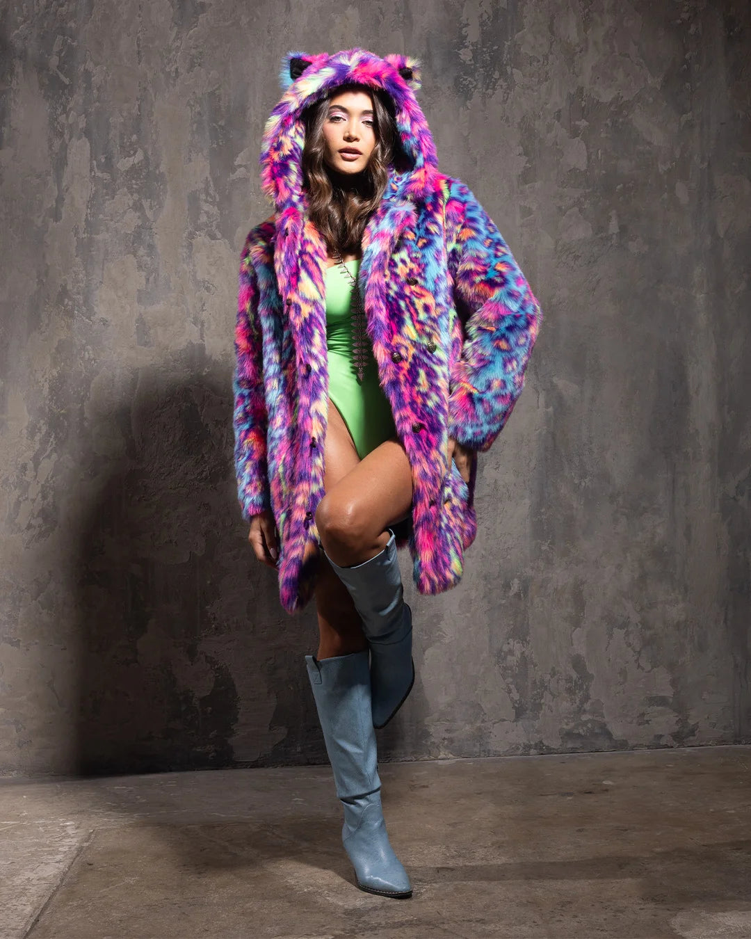 Person wearing a colorful neon fake fur coat with cat ears, green outfit, and blue knee-high boots against a gray background.
