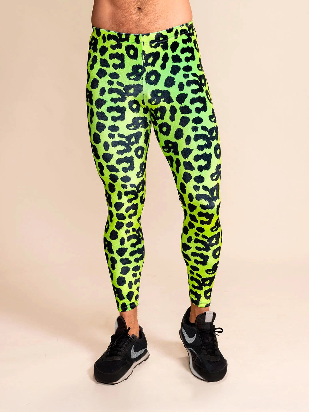 Man wearing neon green leopard print velvet leggings with a black faux fur coat over his shoulder against a gray background