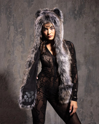 Woman wearing a grey wolf fake fur spirit hood with a hood, ears, and paws, against a textured gray background