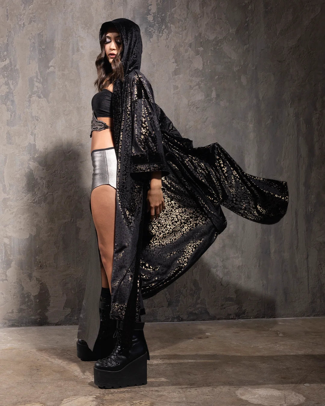Woman with her arms out, wearing a hooded black kimono with golden metallic cheetah print throughout in front of a textured grey wall
