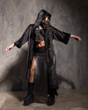 Woman with her arms out, wearing a hooded black kimono with golden metallic cheetah print throughout in front of a textured grey wall