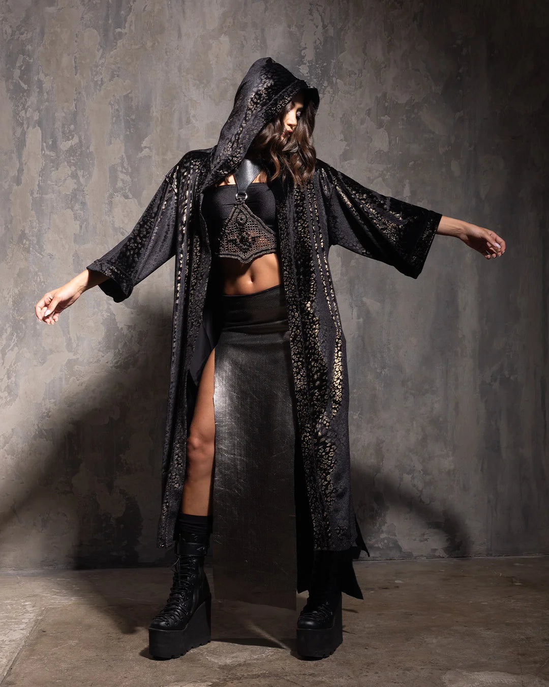 Woman with her arms out, wearing a hooded black kimono with golden metallic cheetah print throughout in front of a textured grey wall