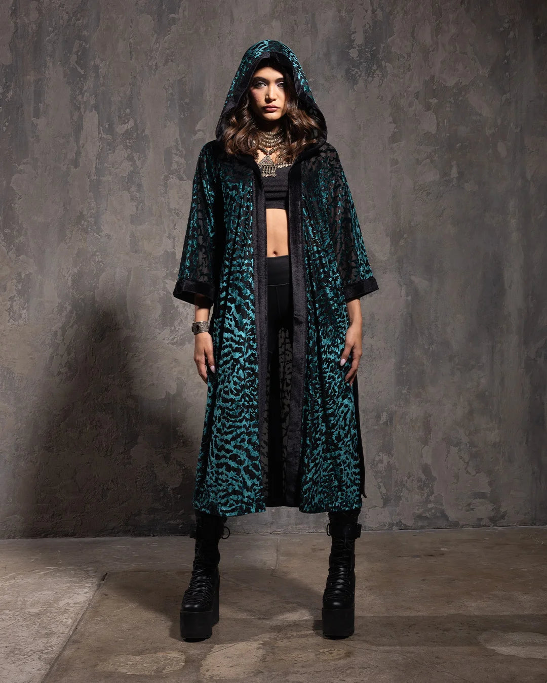 Woman wearing a long, emerald green kimono robe with a hood against a gray background