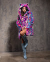 Woman wearing a colorful, leopard print fake fur coat with neon colors throughout against a gray background