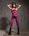 Woman in a pink strapless bodysuit and black platform boots against a textured gray wall.