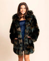 Woman wearing a multi-color patchwork army hue green camo faux fur coat with a neutral background, smiling with her hands in the front two pockets of the plush vegan jacket.
