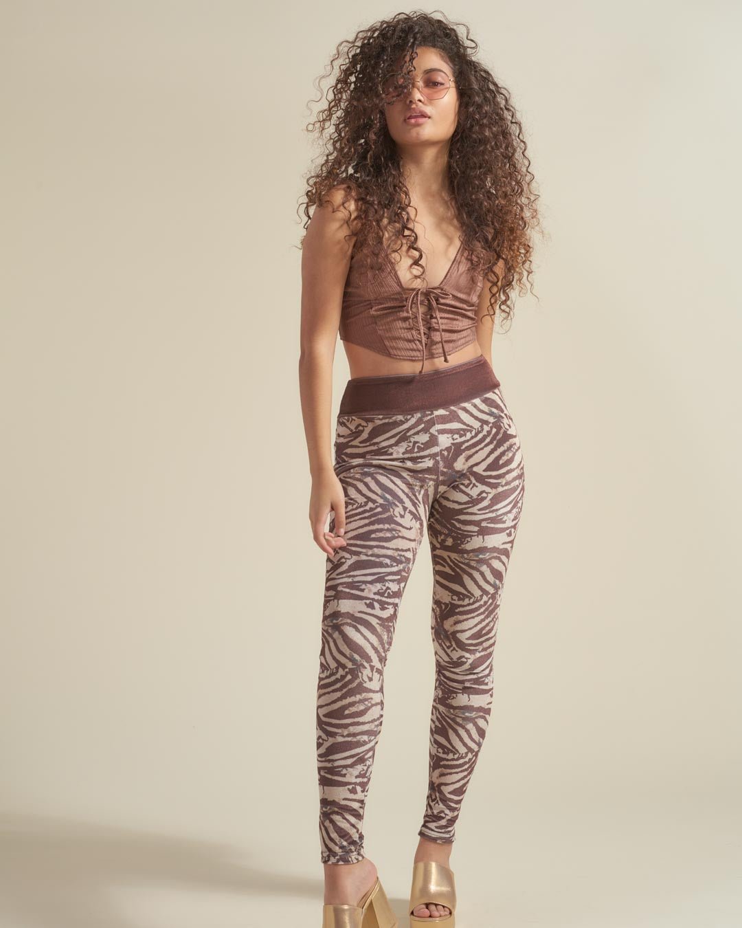 Woman wearing a brown top and zebra print leggings against a beige background