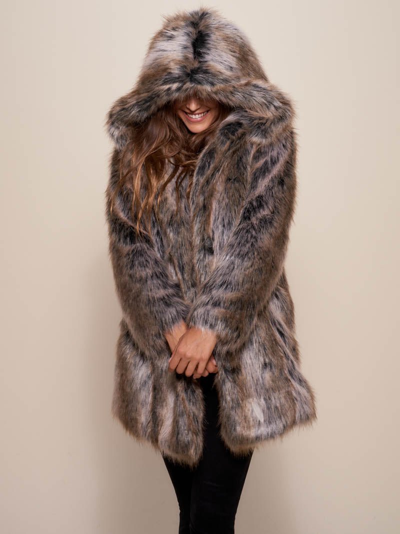 Smiling dark haired female model leaning against a painting while wearing hooded grey wolf fake fur coat.