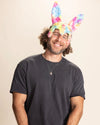 Man wearing a black t-shirt and rainbow tie-dye bunny ear mask against a beige background