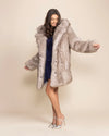 A Woman dancing in a heavyweight silvery grey faux fur winter coat with her arms out, looking happy.