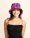 Woman smiling wearing a raspberry pink fuzzy bucket hat with black tiger print on a beige background