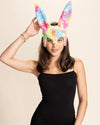 Woman wearing colorful pastel bunny ear mask in rainbow fake fur against a beige background