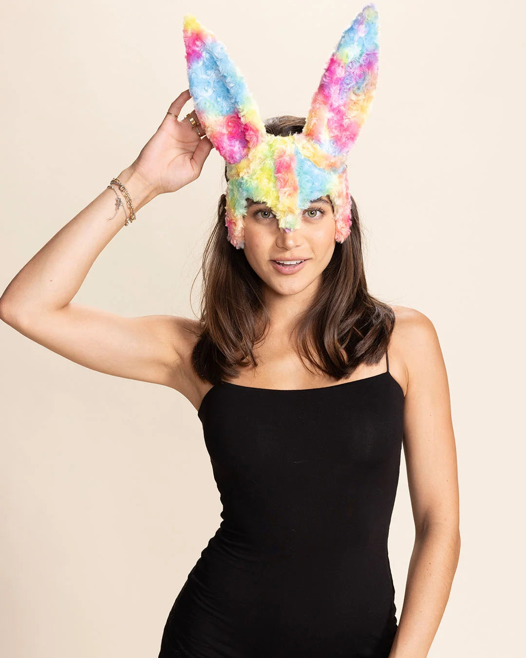 Woman wearing colorful pastel bunny ear mask in rainbow fake fur against a beige background