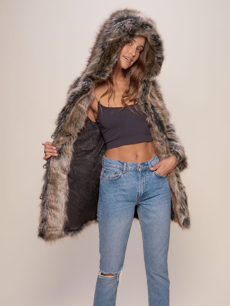 Smiling dark haired female model leaning against a painting while wearing hooded grey wolf fake fur coat.