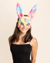 Woman wearing a colorful pastel rainbow bunny mask with large bunny ears on a beige background
