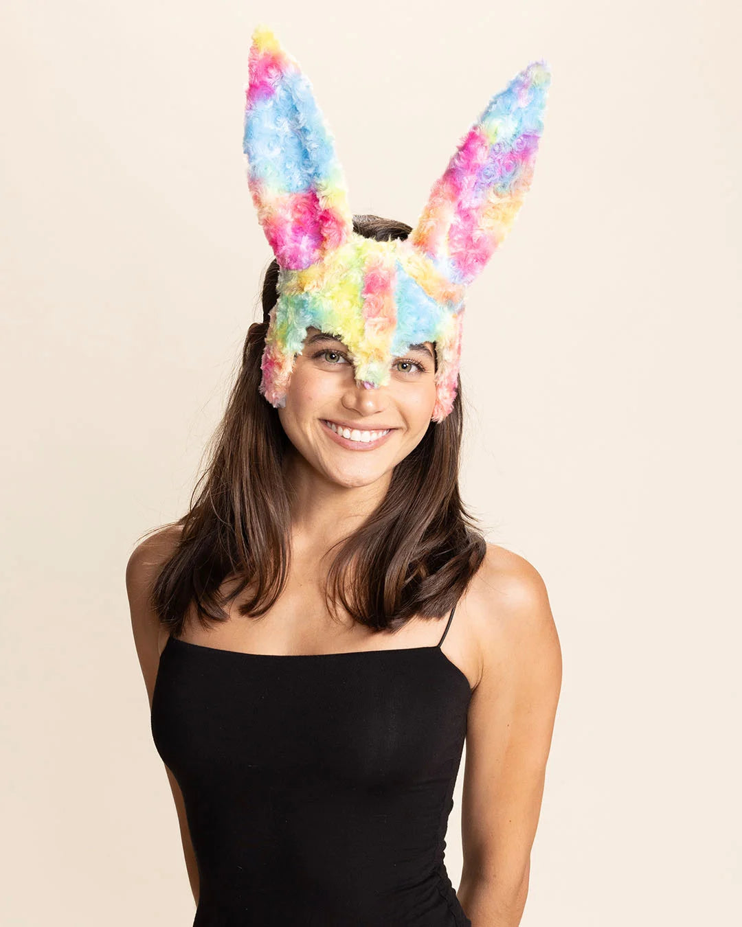 Woman wearing a colorful pastel rainbow bunny mask with large bunny ears on a beige background