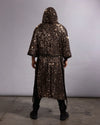 A person viewed from the back wearing a long, hooded kimono robe covered in dense metallic sequins, standing against a plain light gray studio backdrop.