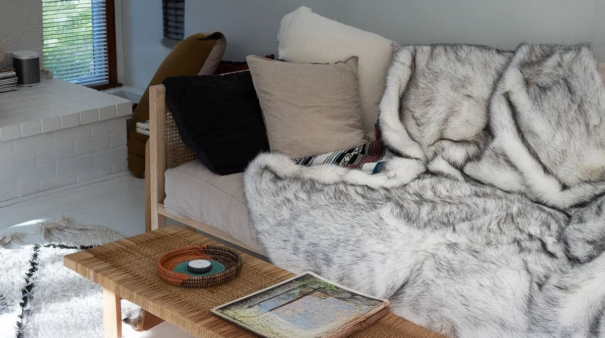 Cozy living room with a sofa covered in a fur throw, cushions, and a small table with a book and bowl.