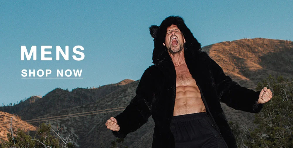 A shirtless man stands triumphantly on the hood of a rusty vintage car in a mountainous desert landscape, wearing a long black faux fur coat with bear ears on the hood. His arms are raised and fists clenched as he yells with intensity. Bold white text at the bottom reads “MENS” with a “SHOP NOW” button underneath.