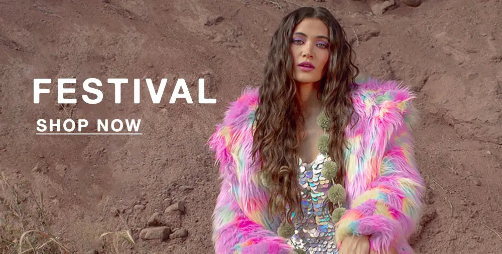 A woman poses against a dusty, rocky backdrop wearing a colorful rainbow faux fur jacket over a sequined top with pom-pom details. Her long wavy hair and bold purple eye makeup complete the vibrant festival look. Bold white text on the left reads “FESTIVAL” with a “SHOP NOW” button beneath it.