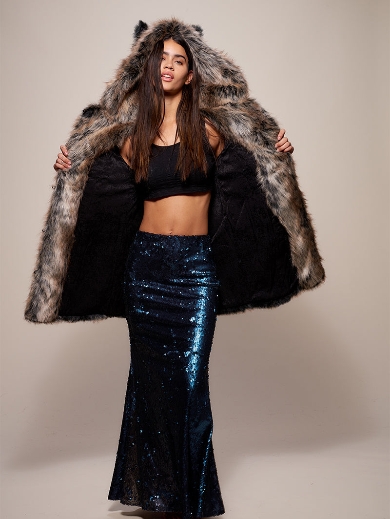 Brunette woman wearing a long blue sequin skirt, a black crop tank top, and a faux fur coat. She is holding the coat open, showing it has a black liner.
