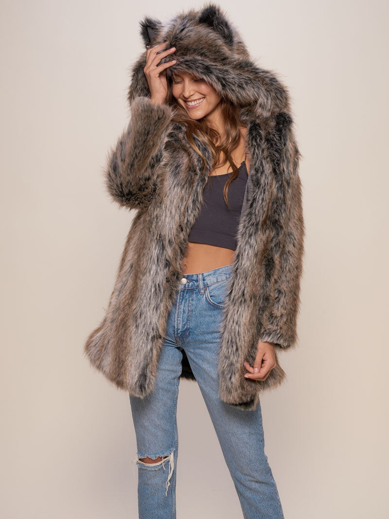 Woman wearing blue jeans, a black crop tank top and a furry hooded coat with one hand touching the hood.